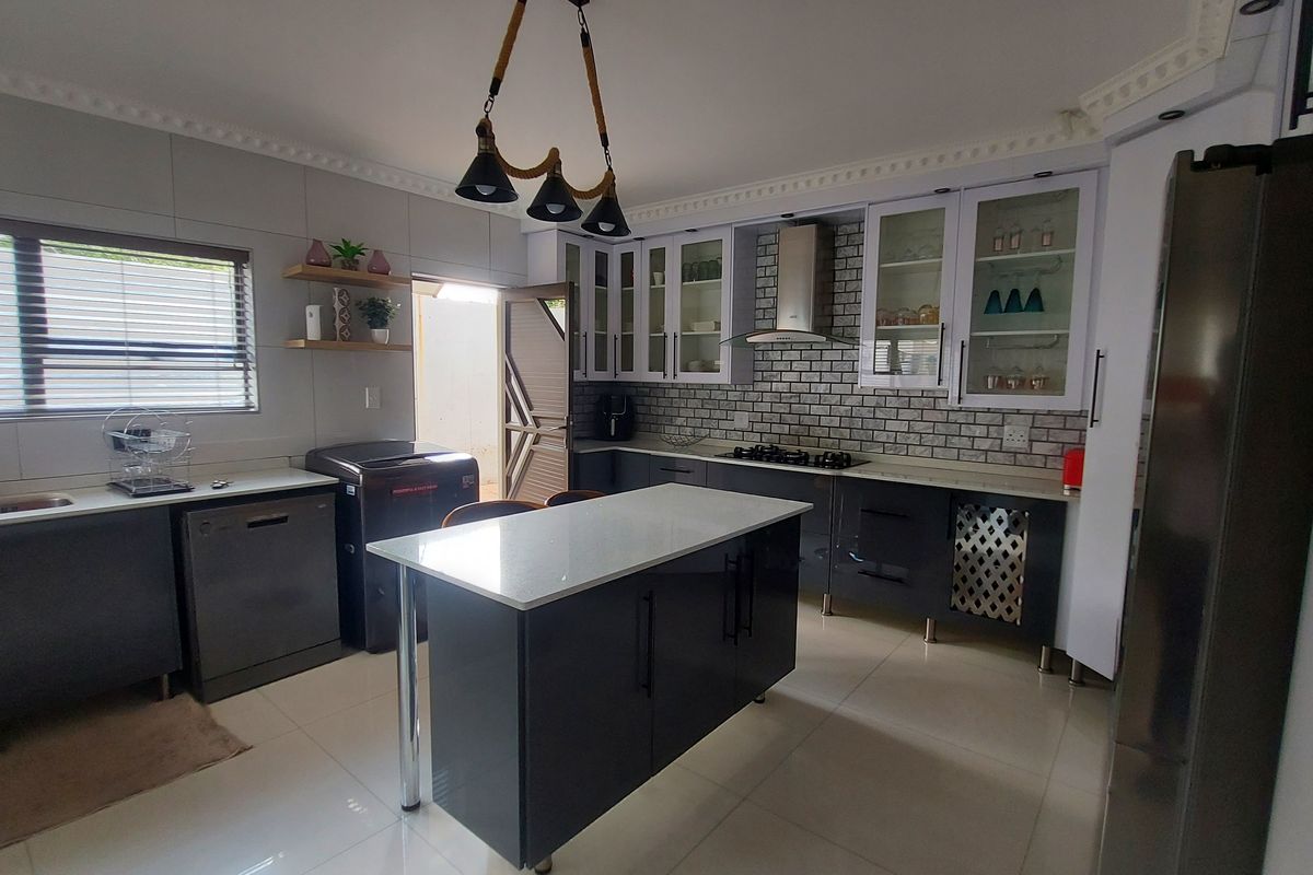 Modern kitchen featuring a central island, stone countertops, dark cabinetry, gas hob, extractor fan, and tiled backsplash with crown molding details.