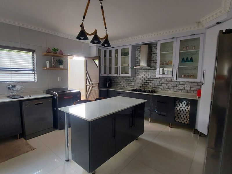Modern kitchen featuring a central island, stone countertops, dark cabinetry, gas hob, extractor fan, and tiled backsplash with crown molding details.