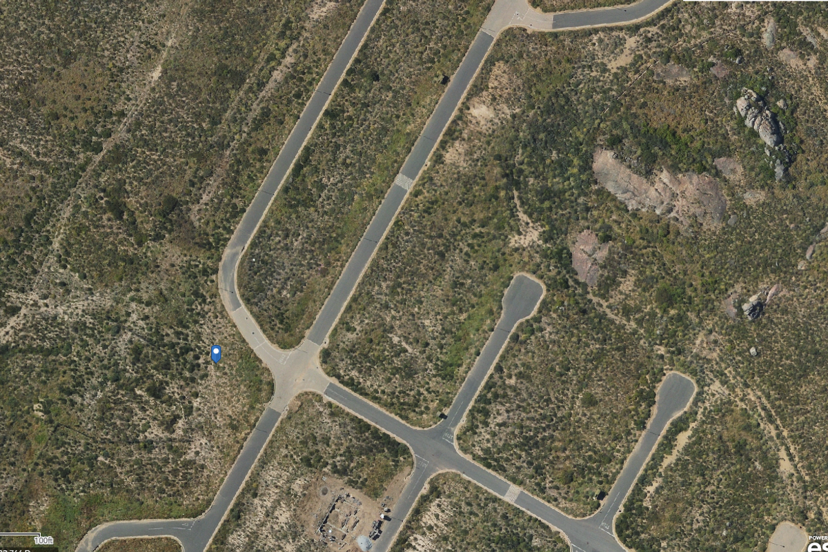 An aerial view of a vacant residential plot situated within a developed estate with established paved road infrastructure.