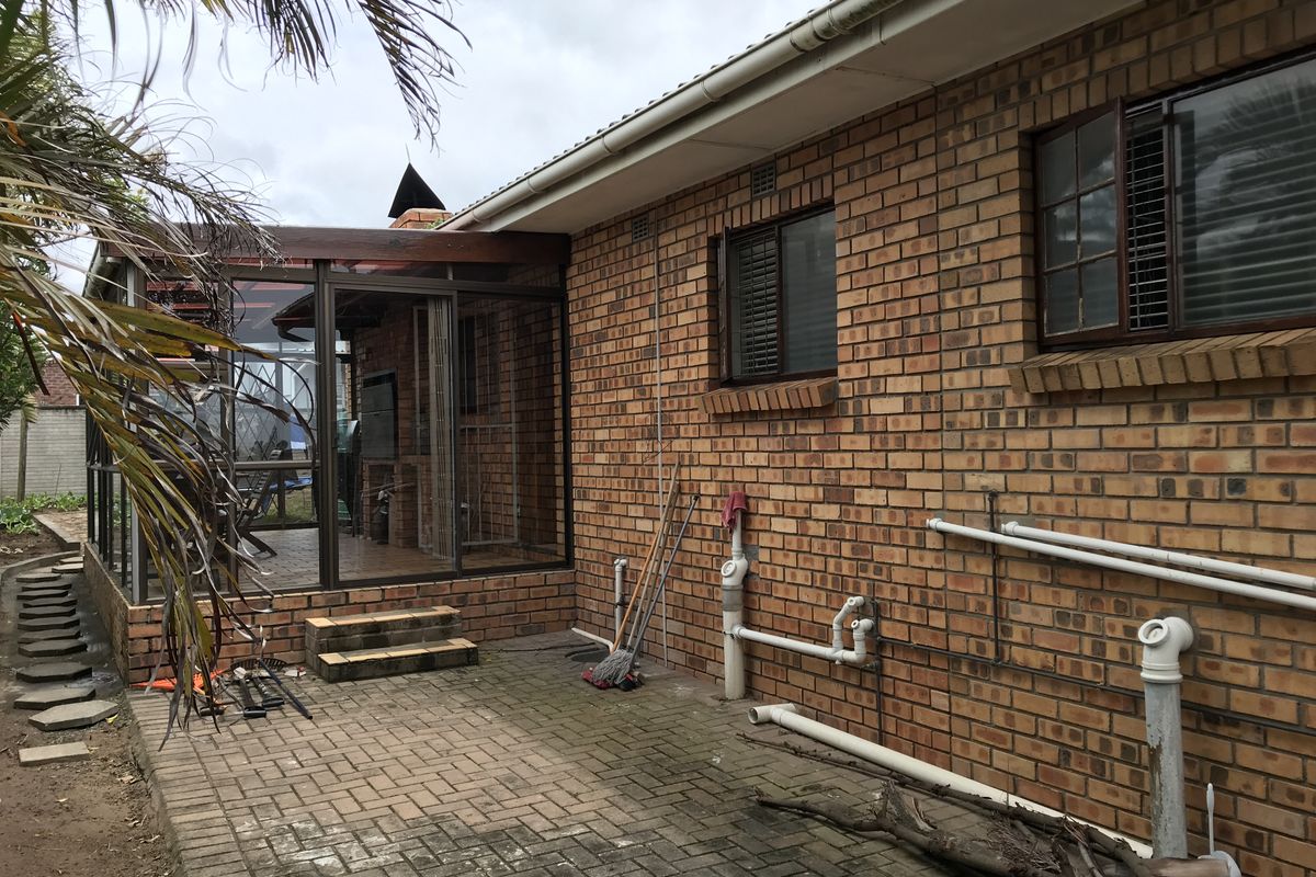 Rear view of the property featuring a brick facade, paved patio area, and an enclosed patio structure with sliding glass doors.