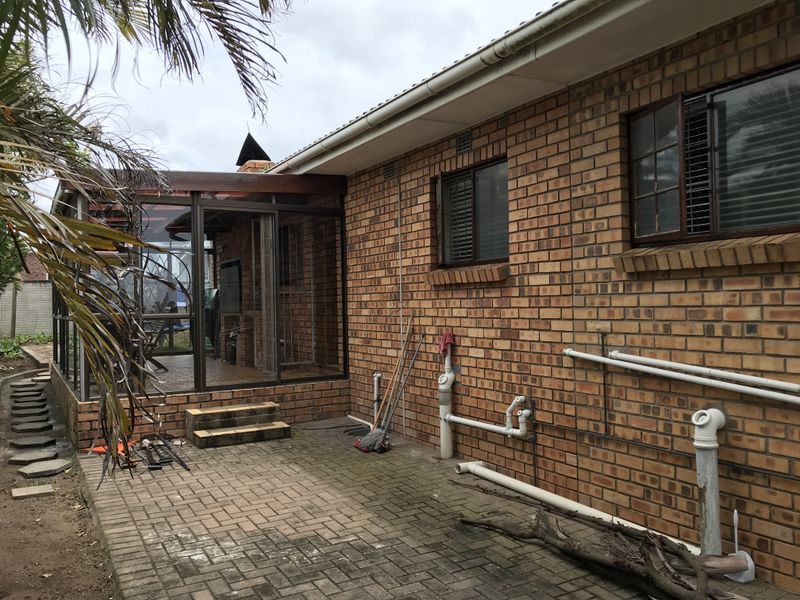 Rear view of the property featuring a brick facade, paved patio area, and an enclosed patio structure with sliding glass doors.