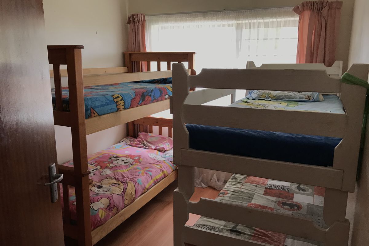 A functional bedroom featuring laminate flooring and a large window, currently configured with multiple bunk beds.