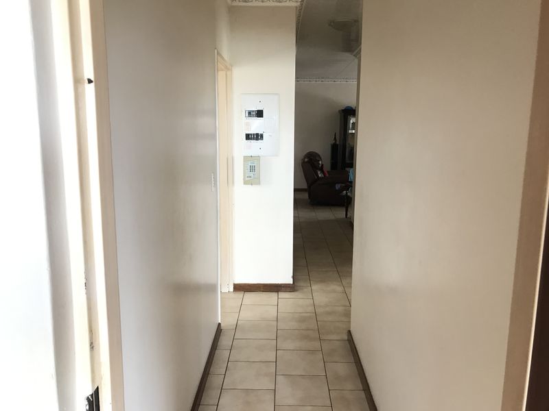 A functional hallway featuring ceramic floor tiles, an integrated electrical distribution board, and an alarm system keypad, leading into the main living area.