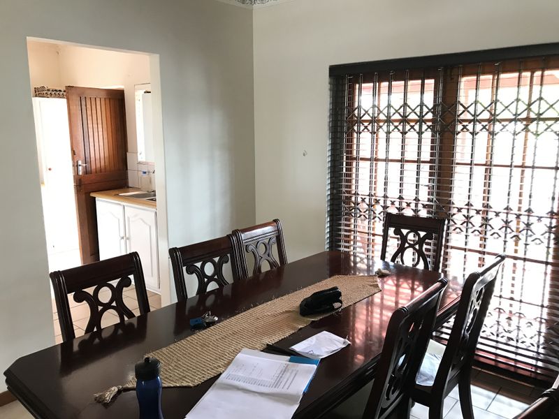 A dining room featuring tiled flooring, a decorative cornice, and a security gate over the glass door, with an adjacent view into a scullery area.