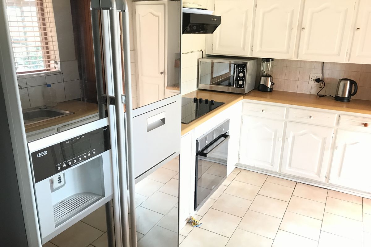 A functional kitchen featuring white cabinetry, laminate countertops, built-in oven, electric hob, and tiled flooring, offering a practical layout for daily meal preparation.