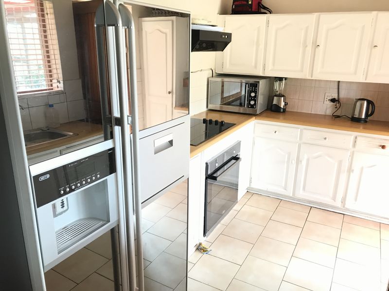 A functional kitchen featuring white cabinetry, laminate countertops, built-in oven, electric hob, and tiled flooring, offering a practical layout for daily meal preparation.