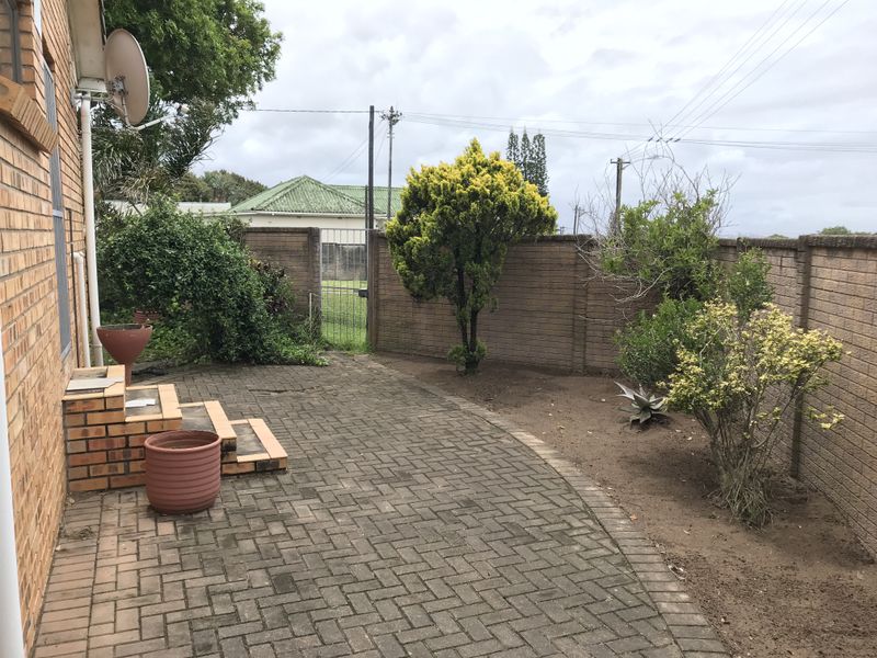 A rear exterior view featuring a brick-paved patio area, brick steps, and a perimeter boundary wall with established garden shrubs.