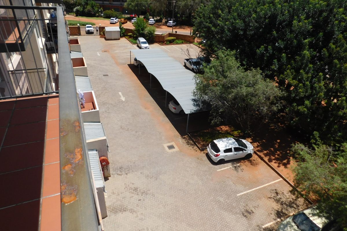 An elevated view of the apartment complex parking area, featuring paved bays, covered carports, and mature trees.