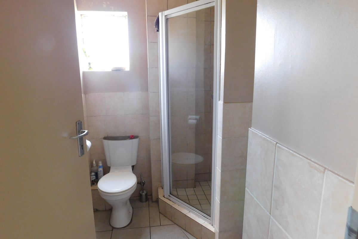 A compact bathroom featuring a shower enclosure, toilet, and neutral wall and floor tiling, requiring some cosmetic maintenance.