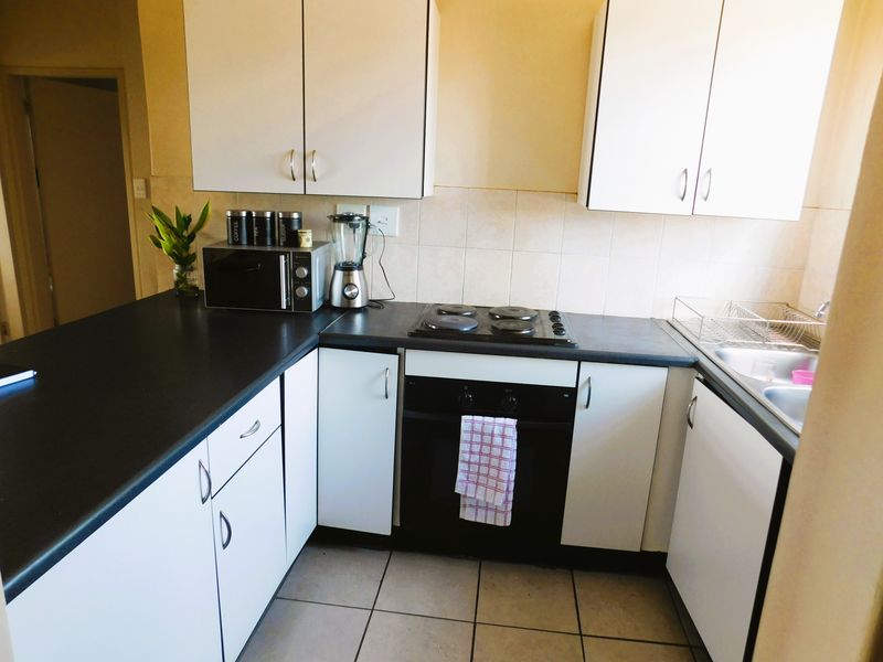 A functional kitchen featuring white cabinetry, dark laminate countertops, an integrated electric hob and oven, and tiled flooring with a neutral backsplash.