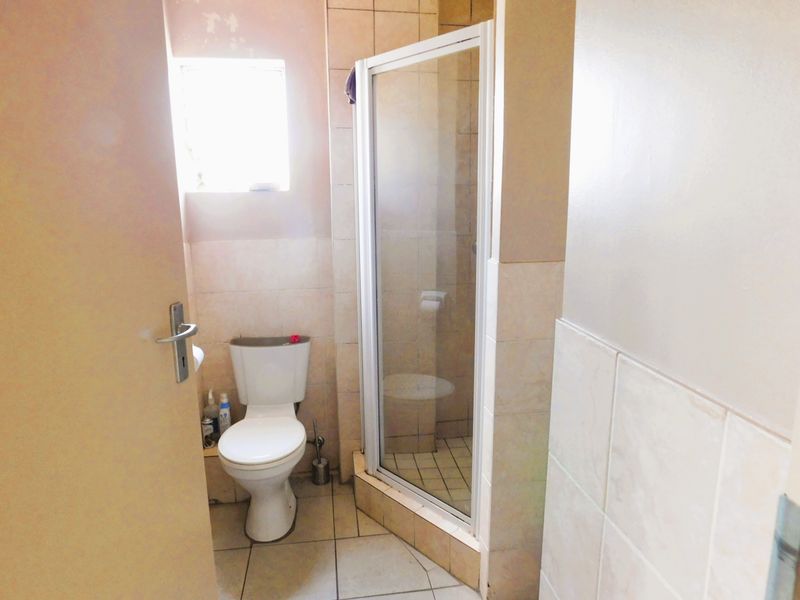 A functional bathroom featuring a corner shower enclosure, a standard toilet, and neutral wall and floor tiling.