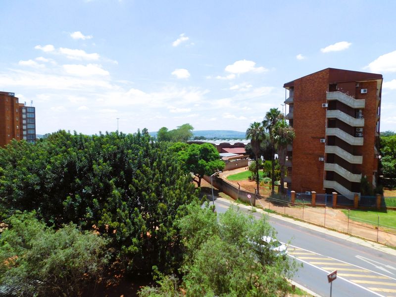 An elevated view overlooking the surrounding neighbourhood, featuring mature trees, a nearby apartment building with external stairwells, and local street infrastructure.
