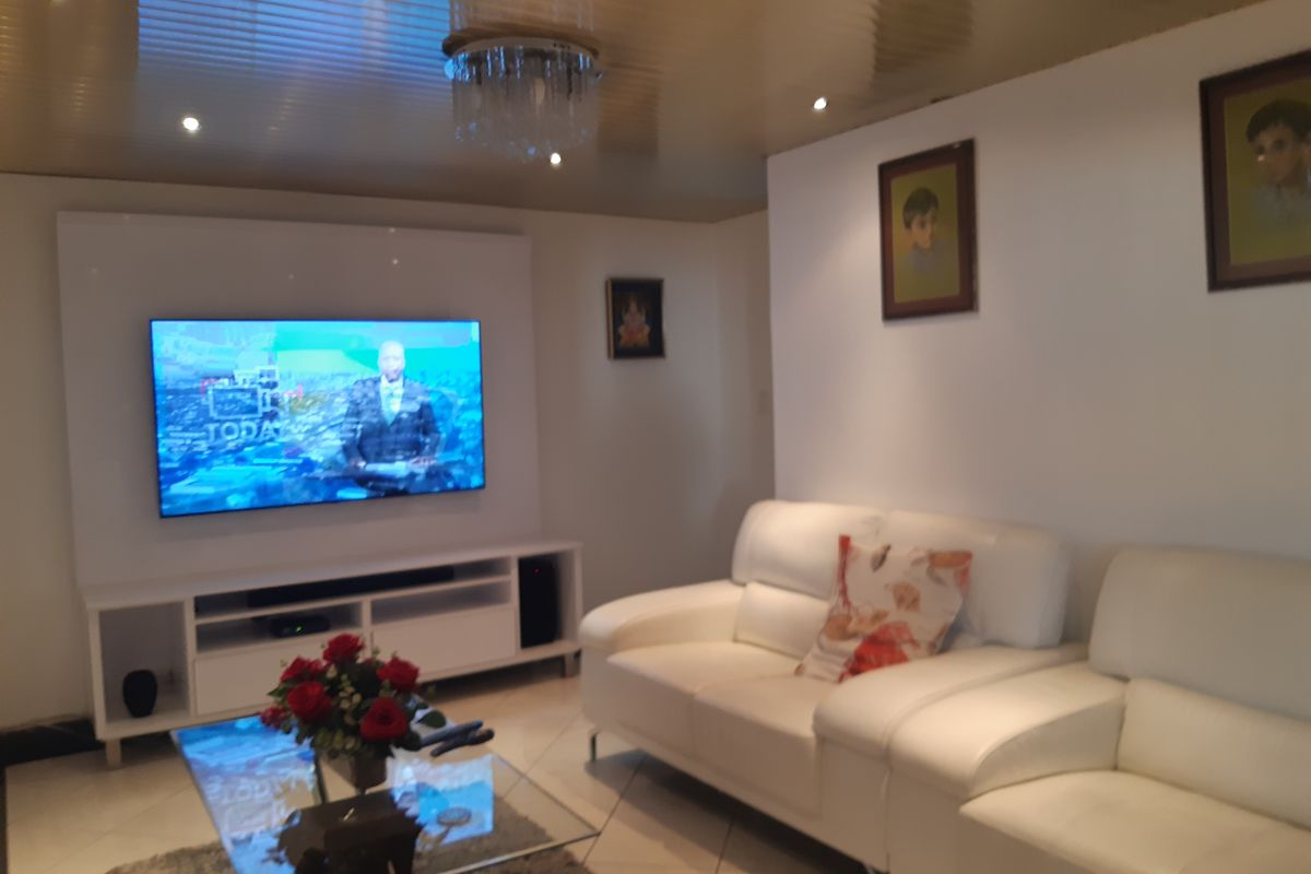 A living room featuring a glossy ceiling finish, recessed downlighting, and tiled flooring, centered around a wall-mounted television unit.