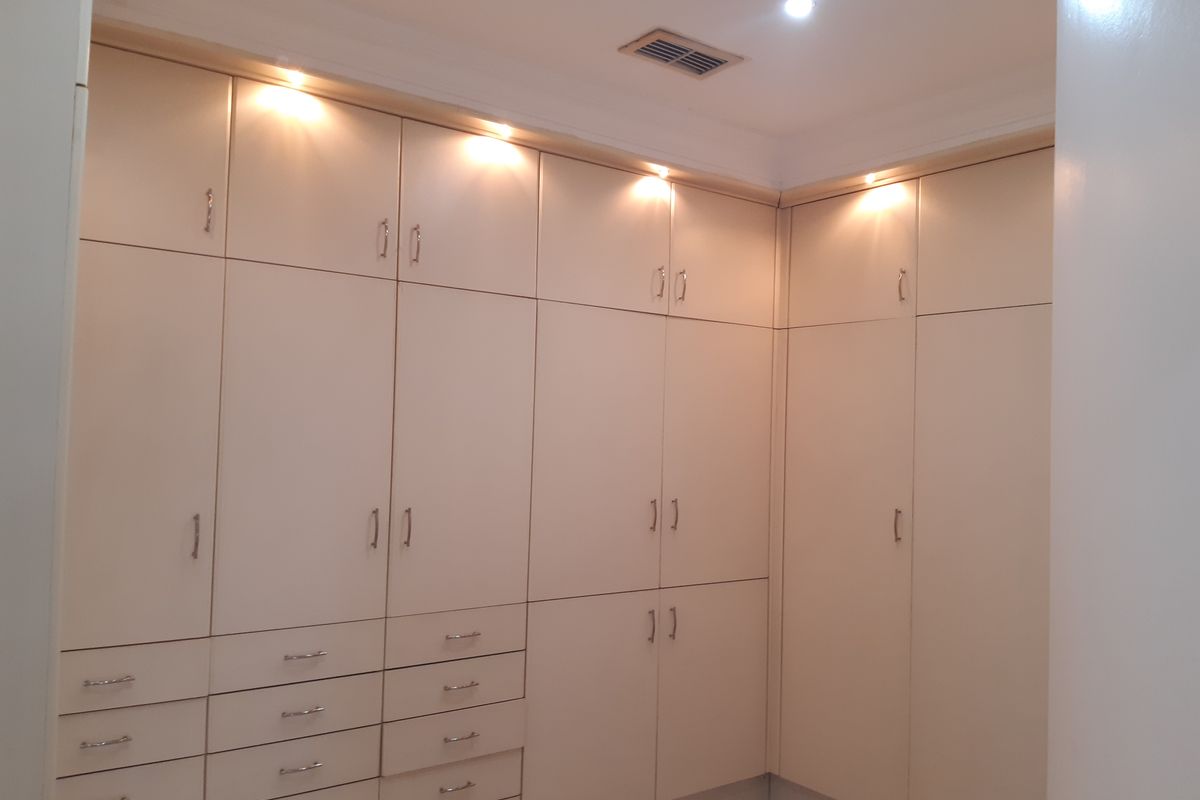 A well-maintained bedroom featuring extensive floor-to-ceiling built-in cabinetry with integrated downlighting and ample storage space.