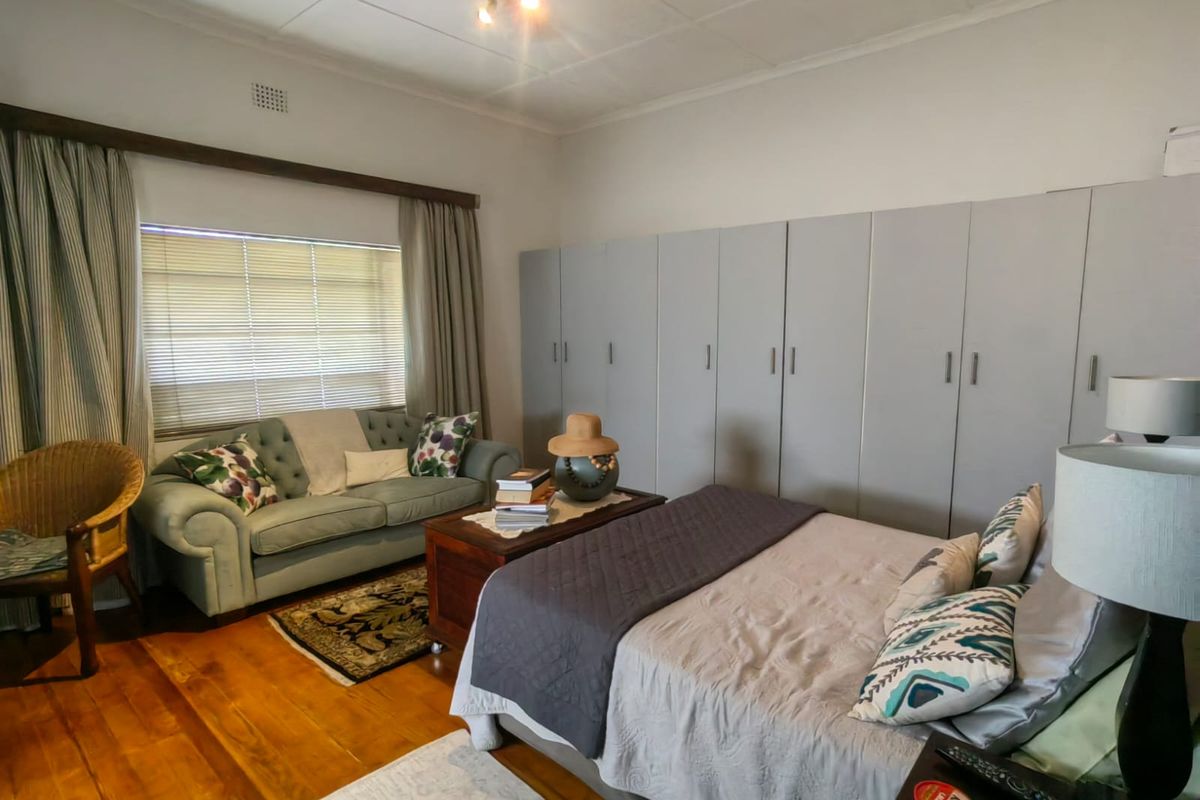 Spacious bedroom featuring polished hardwood flooring, extensive built-in cupboard storage, and a ceiling fan, offering a comfortable and functional living space.