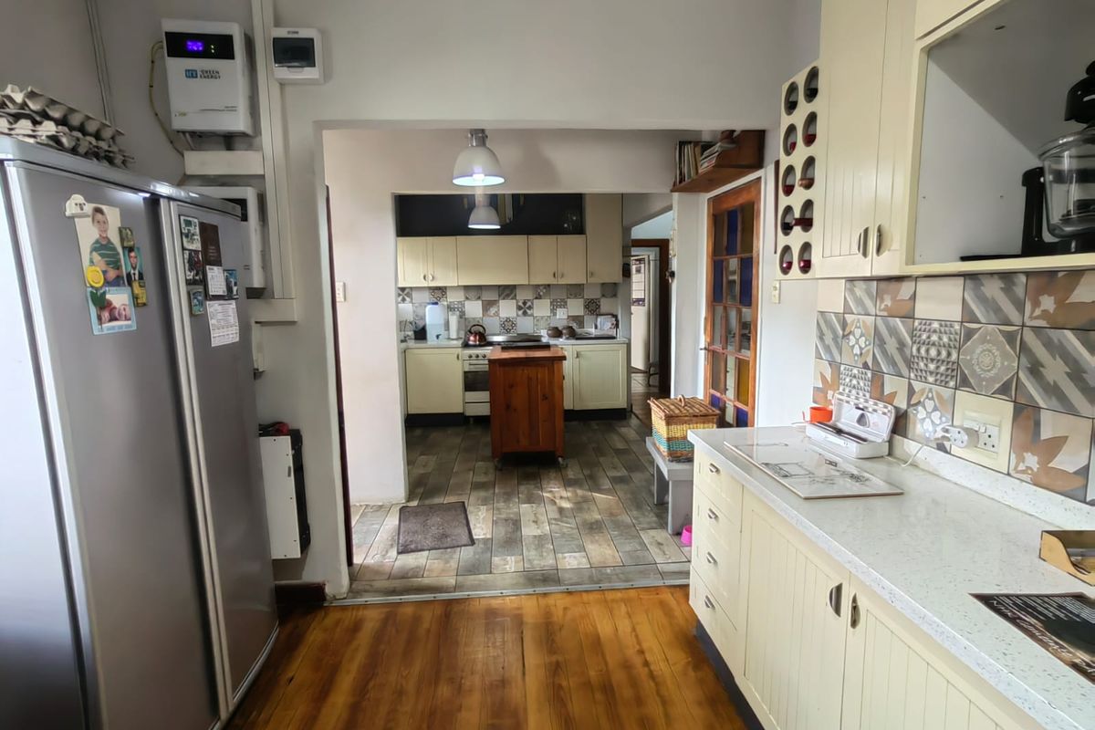 A functional kitchen featuring built-in cabinetry, stone countertops, and a decorative tiled backsplash, with a connected scullery area and timber flooring.