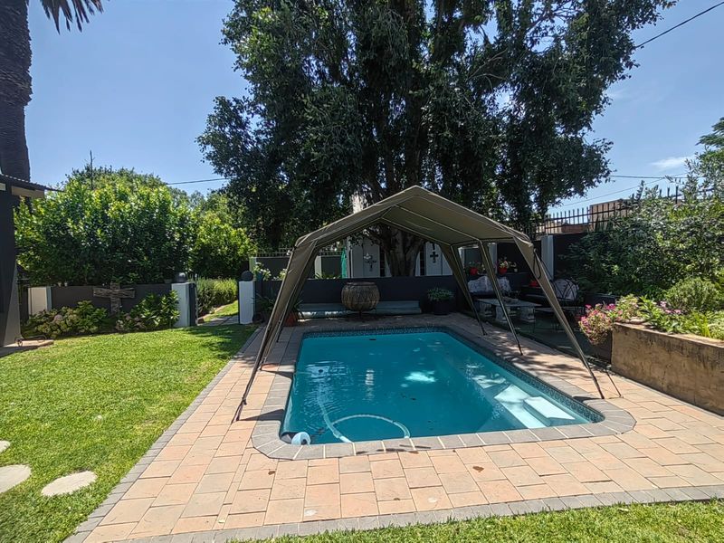 A private swimming pool area featuring a paved surround, established garden, and boundary wall, providing a pleasant outdoor space for relaxation.