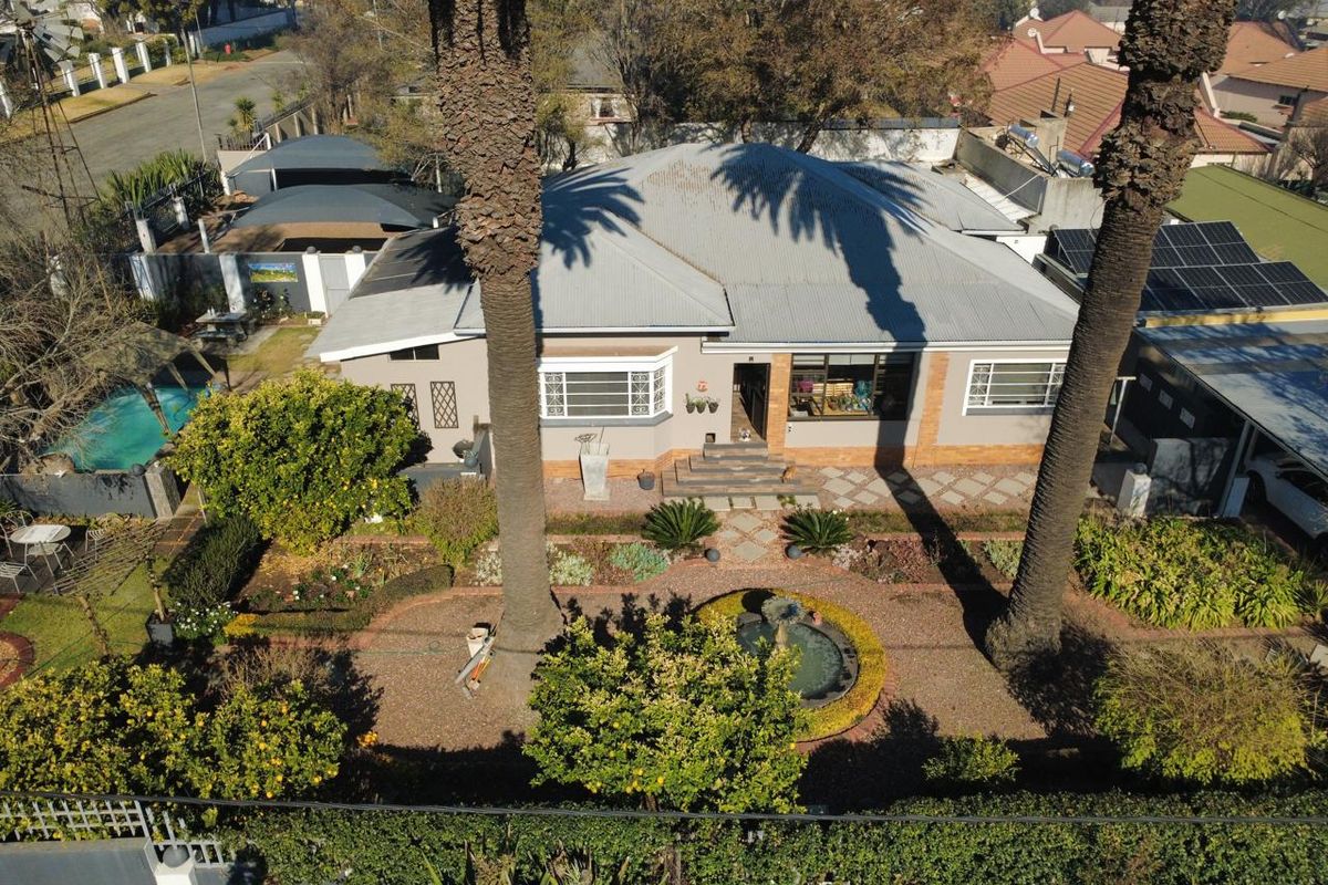 Aerial view of a residential property featuring a landscaped garden with a central fountain, swimming pool, solar panels, and a paved driveway.