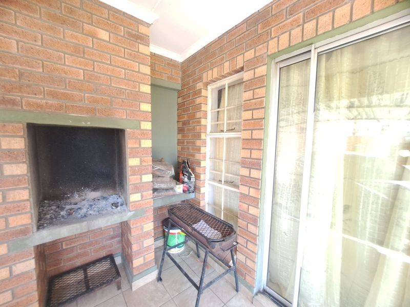A covered patio area featuring a built-in brick braai, tiled flooring, and sliding glass door access to the interior living space.