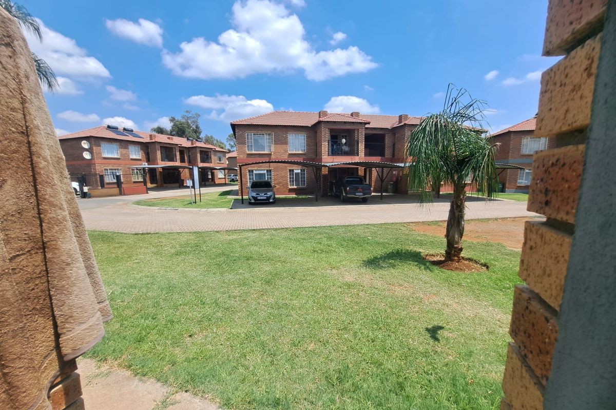 Exterior view of a face brick apartment complex featuring paved driveways, covered carports, and well-maintained communal garden areas.