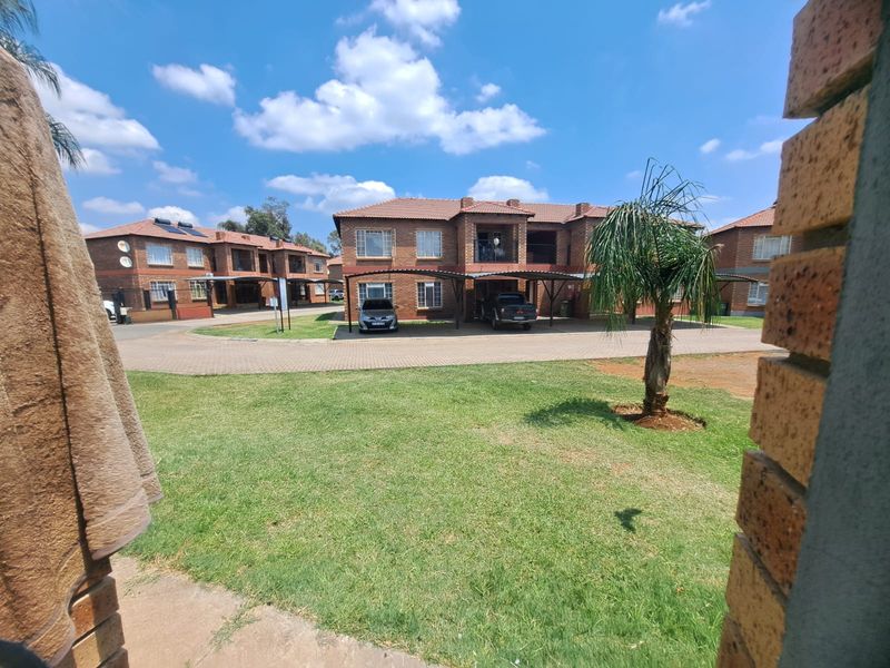 Exterior view of a face brick apartment complex featuring paved driveways, covered carports, and well-maintained communal garden areas.