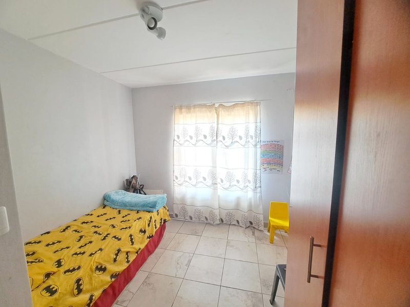 A functional bedroom featuring tiled flooring, a built-in cupboard, and natural light through a window with curtains.