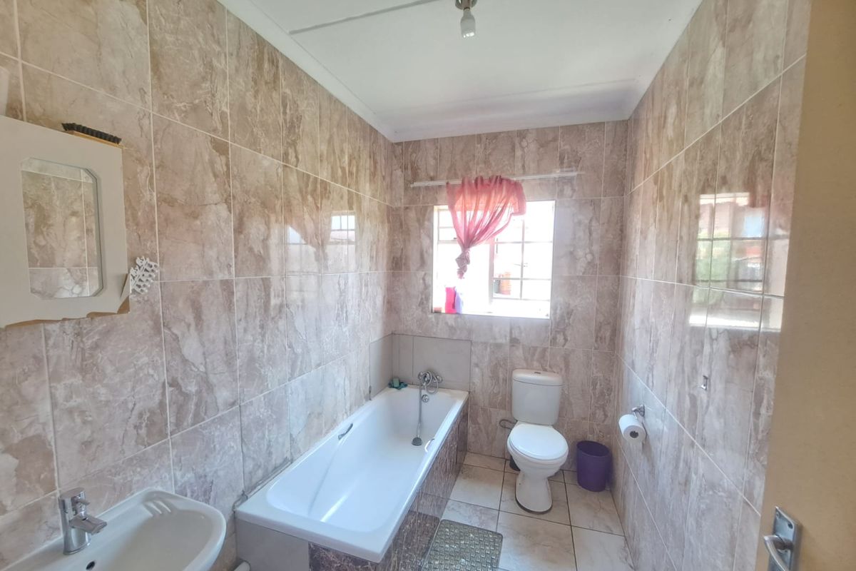 A functional bathroom featuring full-height marble-look wall tiles, a standard bathtub, a toilet, and a wall-mounted washbasin.