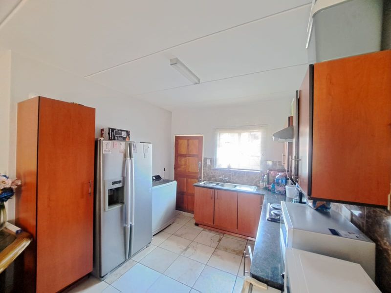 A functional kitchen featuring built-in wooden cabinetry, a double sink, tiled flooring, and a tiled backsplash, offering a practical layout for daily use.
