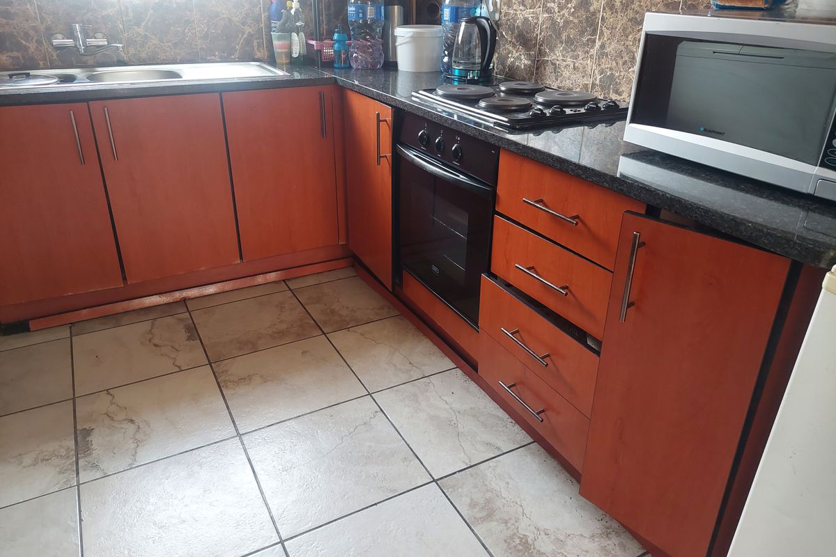 A functional kitchen featuring laminate cabinetry, granite countertops, a built-in oven, electric hob, and tiled flooring with a tiled backsplash.