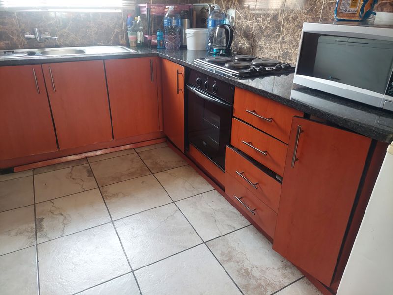 A functional kitchen featuring laminate cabinetry, granite countertops, a built-in oven, electric hob, and tiled flooring with a tiled backsplash.