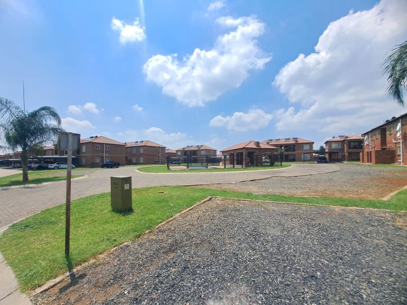 A wide-angle view of a residential apartment complex featuring multiple brick buildings, paved driveways, and communal outdoor spaces under a clear sky.
