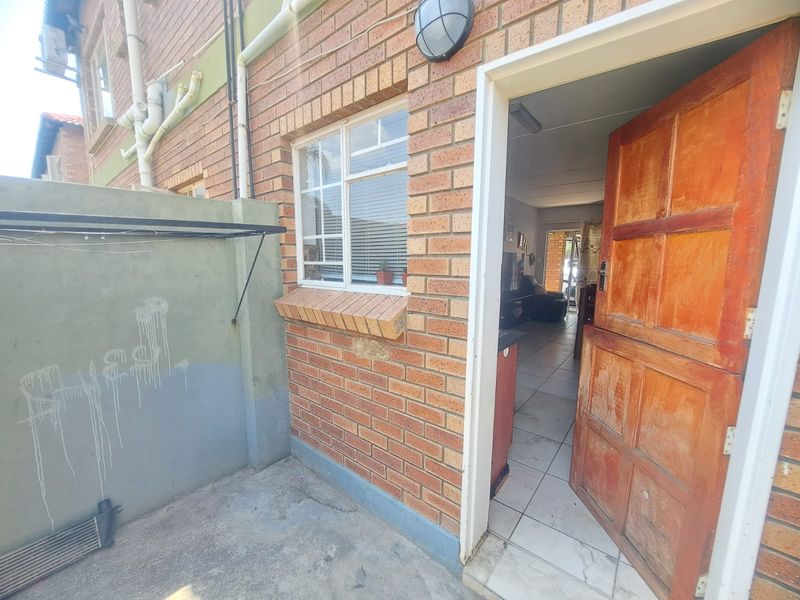 Rear exterior view of the apartment featuring a face brick facade, timber entrance door, and a small concrete patio area.
