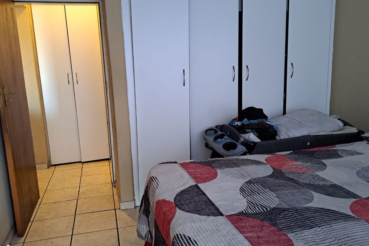 A bedroom featuring built-in white wardrobes and tiled flooring, with an adjacent hallway entrance.