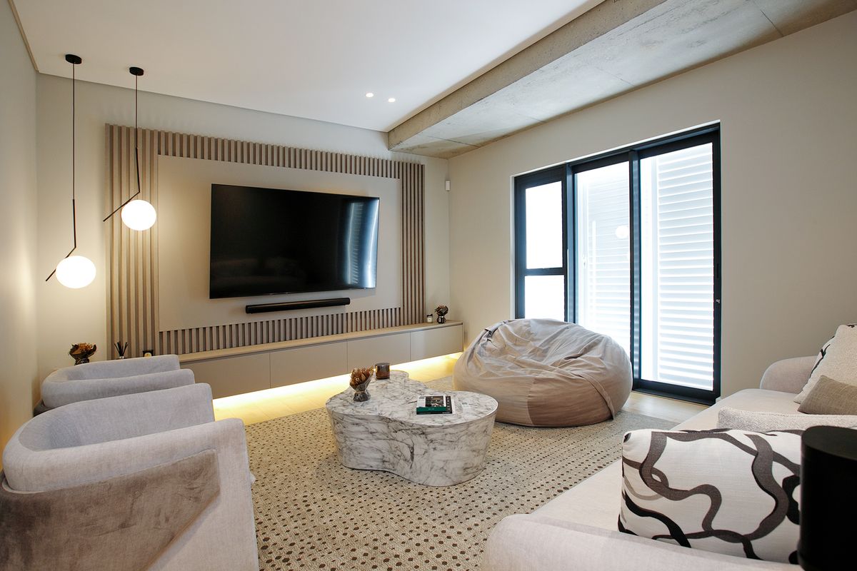 Modern living room featuring a custom slatted timber feature wall with integrated cabinetry, recessed LED lighting, and exposed concrete ceiling detail.
