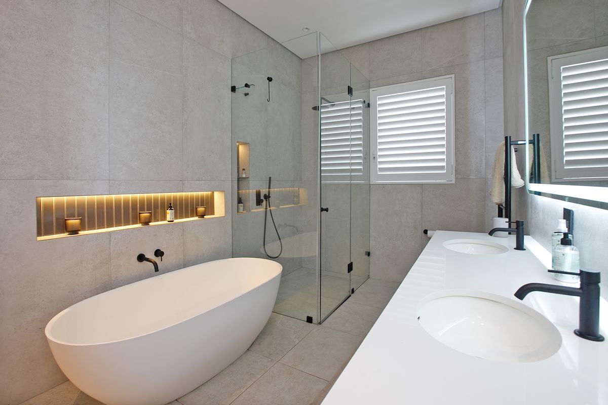 Modern bathroom featuring a freestanding bathtub, frameless glass shower enclosure, double vanity with matte black fixtures, and integrated LED wall niche lighting.
