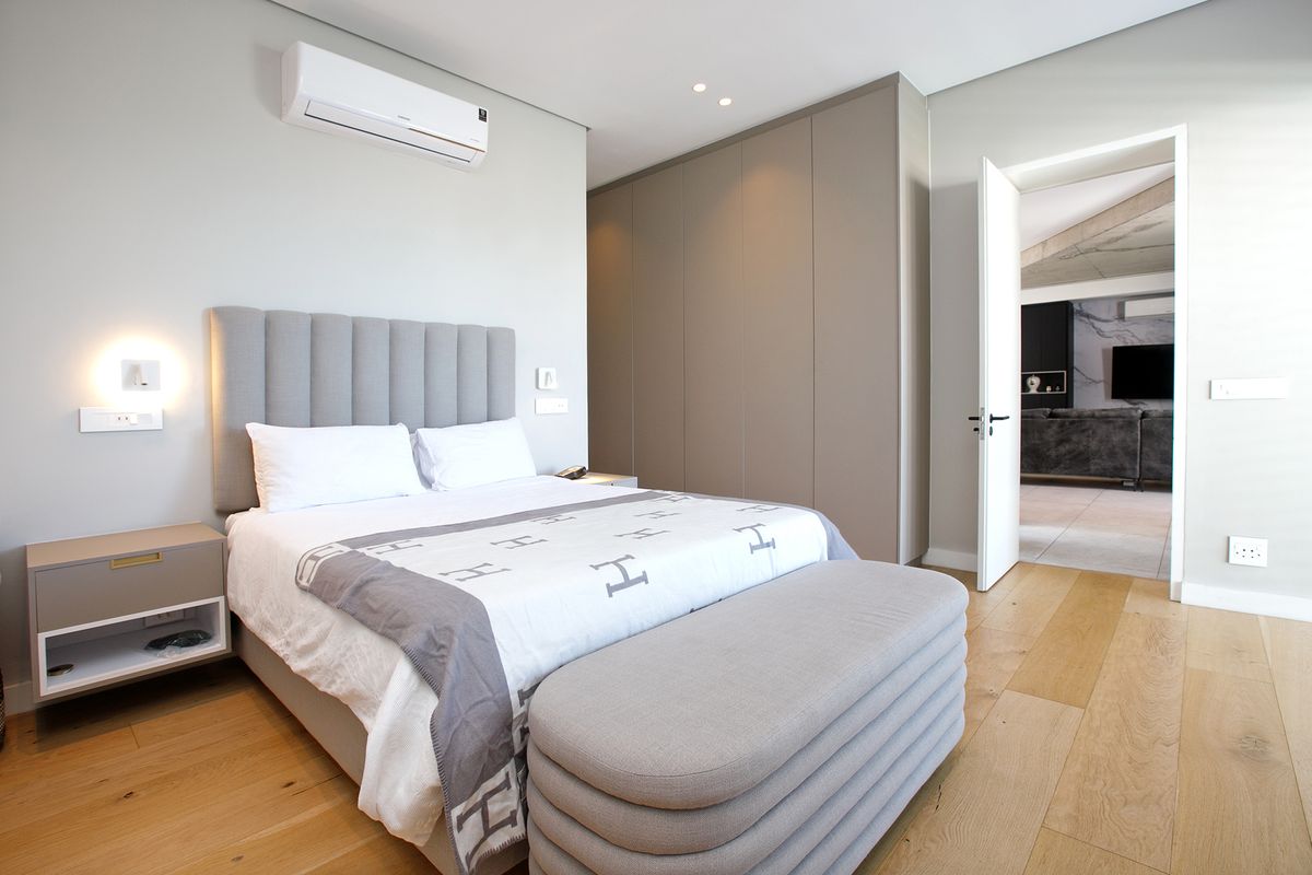 Modern bedroom featuring light timber flooring, built-in floor-to-ceiling cabinetry, recessed lighting, and a wall-mounted air conditioning unit.