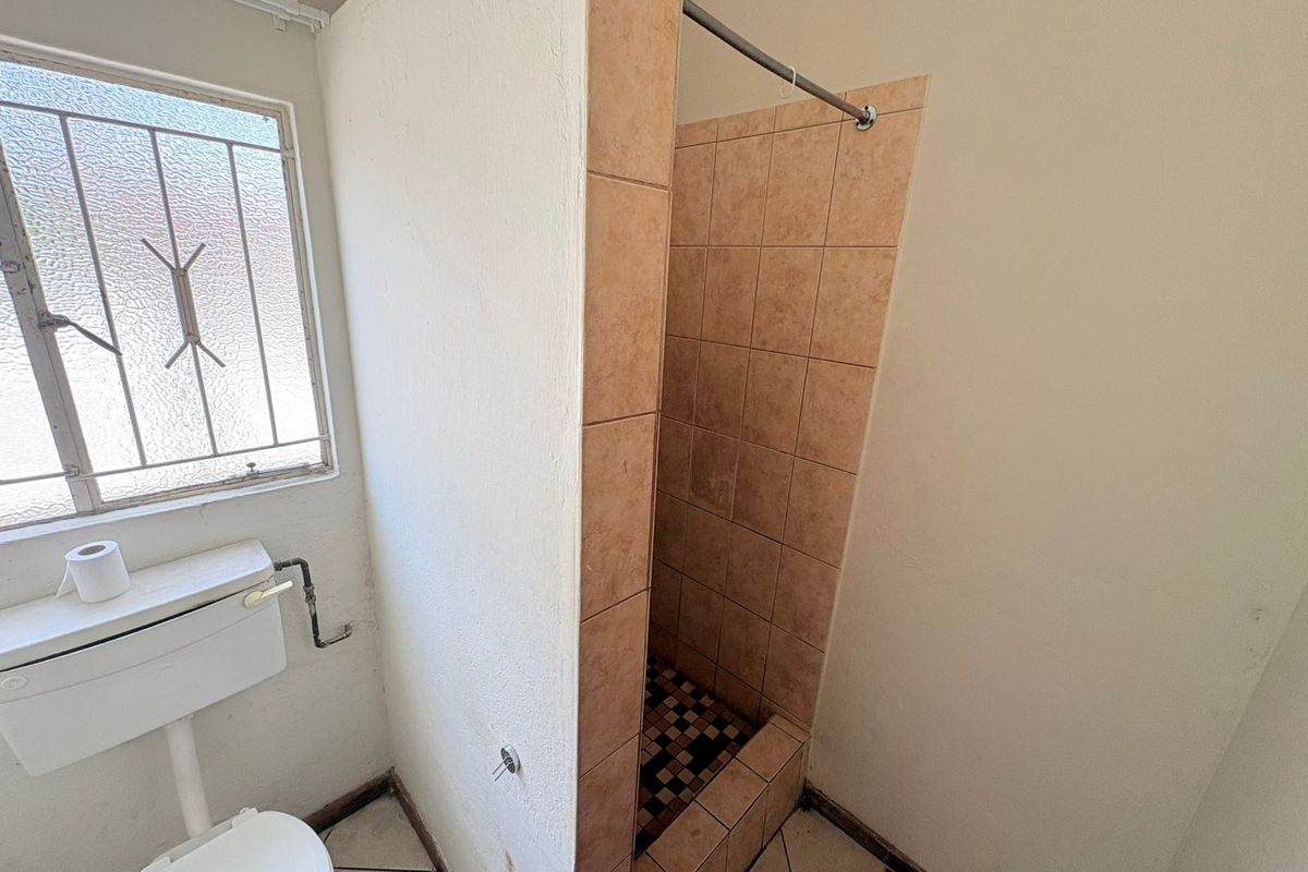 A functional bathroom featuring a tiled shower cubicle, toilet, and security-barred window. The space requires cosmetic updates to modernize the dated finishes.