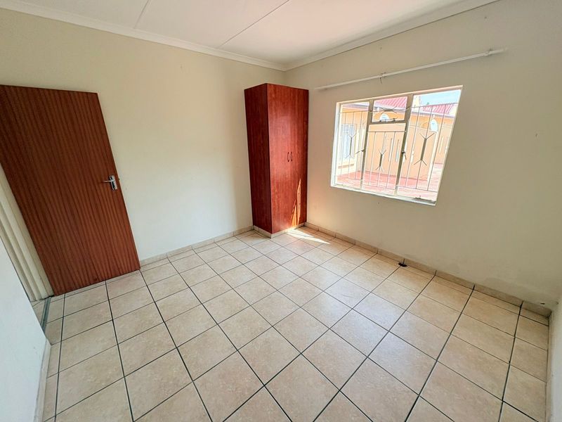 A simple, empty bedroom featuring tiled flooring, a built-in wardrobe, and a window fitted with security bars.