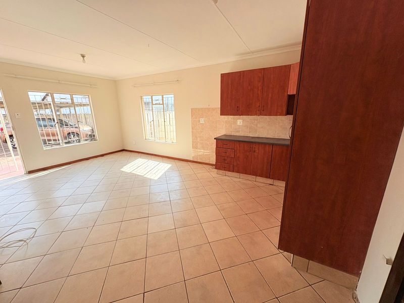 Open-plan living area featuring tiled flooring and a compact kitchen with built-in cabinetry and tiled backsplash, offering a functional blank canvas.