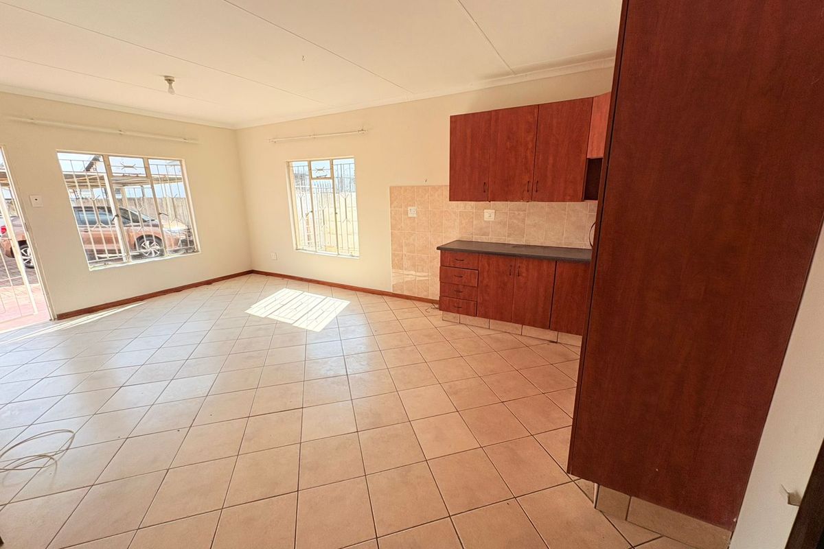 Open-plan living area featuring tiled flooring and a compact kitchen with built-in cabinetry and tiled backsplash, offering a functional blank canvas.