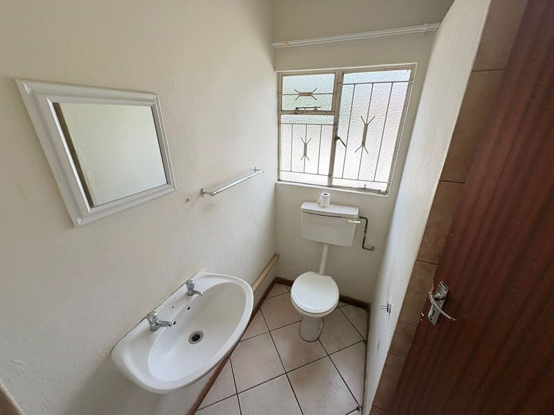 A compact bathroom featuring a pedestal basin, toilet, and tiled flooring, with security bars on the window.