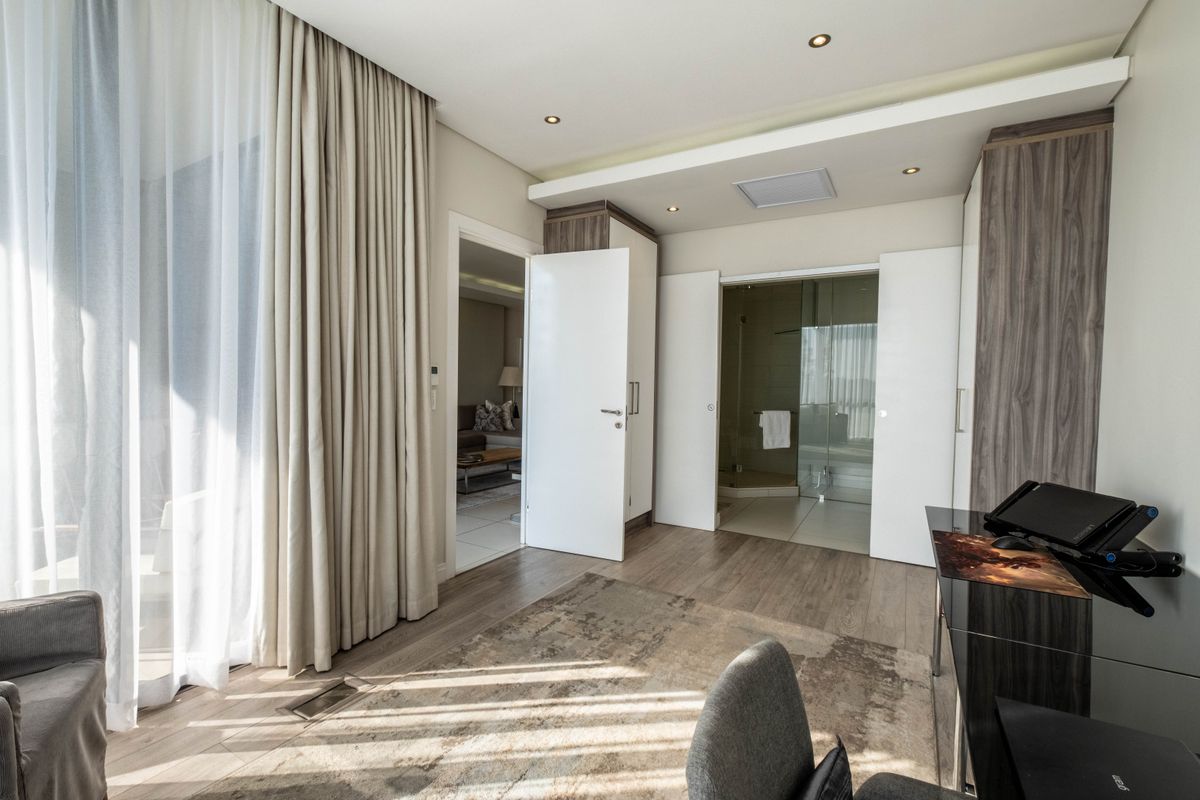 A modern bedroom featuring built-in cabinetry, recessed ceiling lighting, and an en-suite bathroom with a glass-enclosed shower.