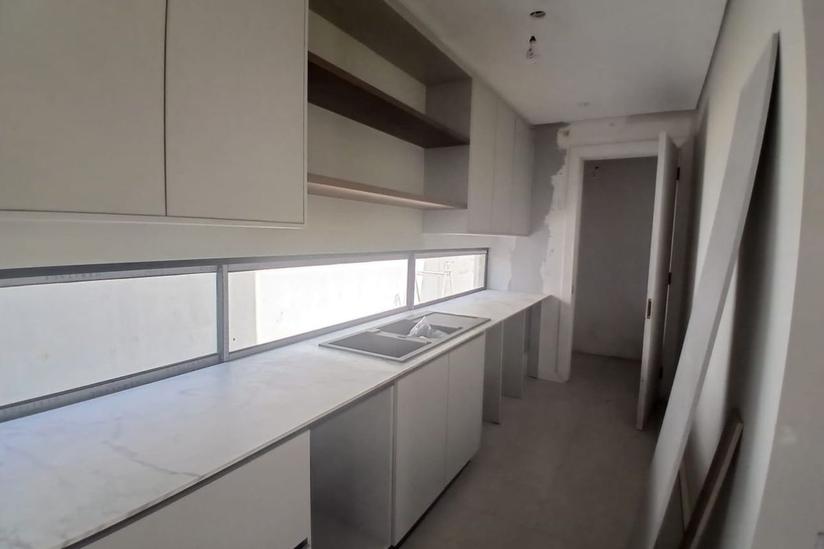 An unfinished kitchen space featuring modern cabinetry, stone countertops, and an integrated sink, currently undergoing final installation and plastering work.