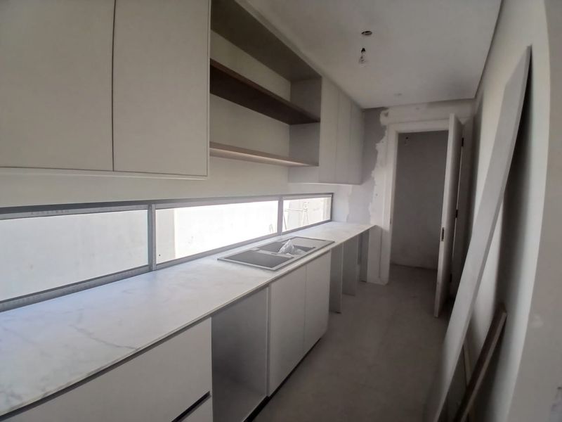 An unfinished kitchen space featuring modern cabinetry, stone countertops, and an integrated sink, currently undergoing final installation and plastering work.