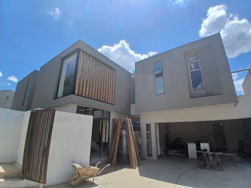 Modern double-story cluster home featuring a contemporary facade with timber slat detailing, large windows, and an integrated double garage currently under final construction.