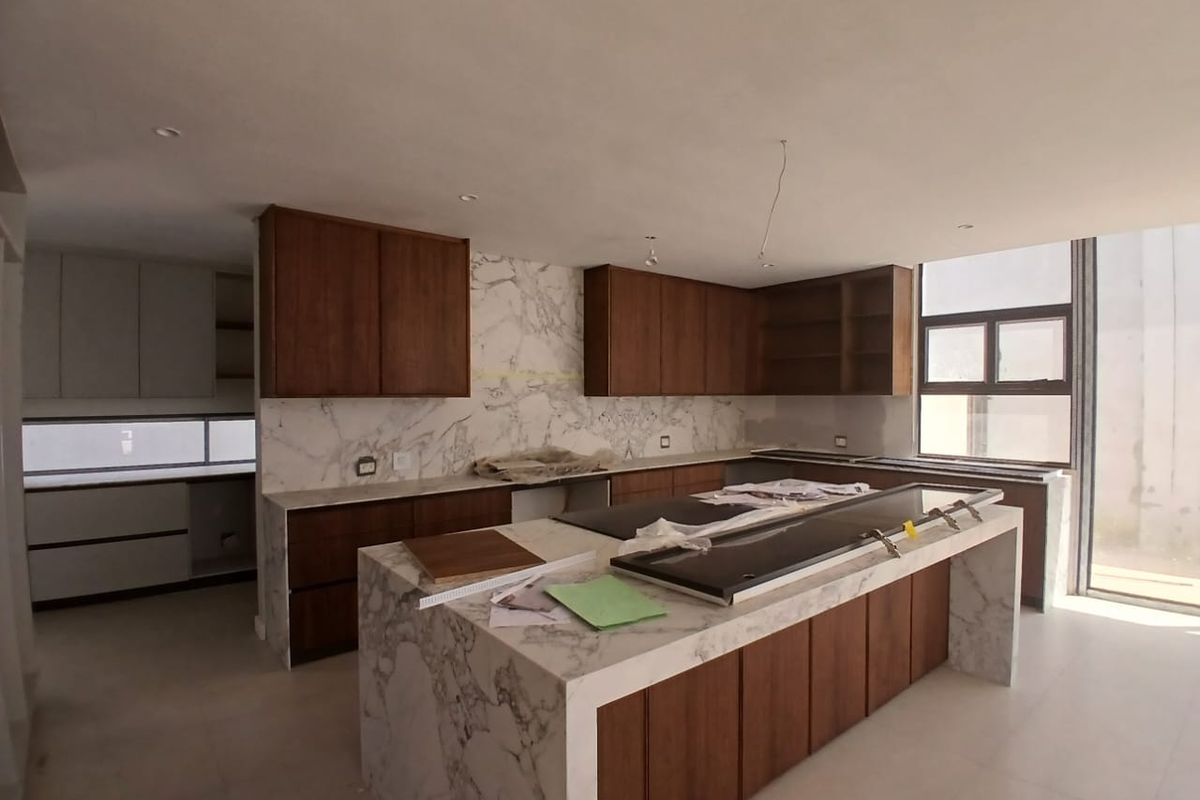 Modern kitchen featuring a marble waterfall island, marble backsplash, and custom wooden cabinetry, currently in the final stages of construction and installation.