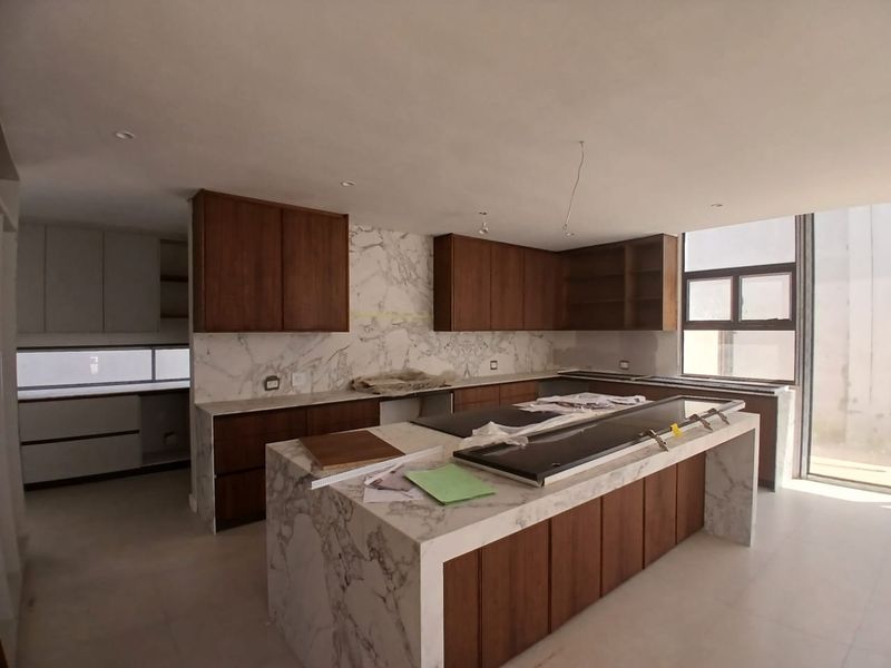 Modern kitchen featuring a marble waterfall island, marble backsplash, and custom wooden cabinetry, currently in the final stages of construction and installation.