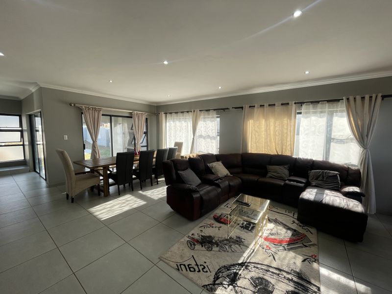 Spacious open-plan living and dining area featuring large windows, sliding glass doors, neutral tiled flooring, and recessed downlighting throughout.