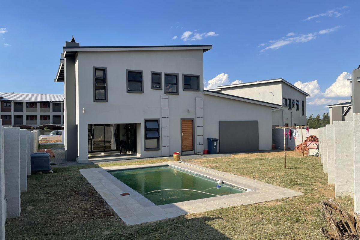 Rear view of a modern two-story house featuring a swimming pool, paved surround, and a private garden area with boundary walls.
