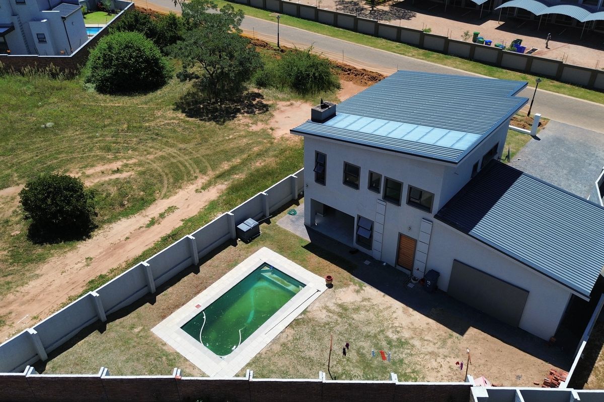 Aerial view of a modern two-story house featuring a swimming pool, metal roofing, and a fully enclosed perimeter wall in a residential estate setting.